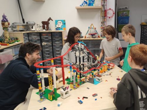 Un animateur Ludi Briques encadre un groupe d'enfants construisant un grand huit en LEGO.