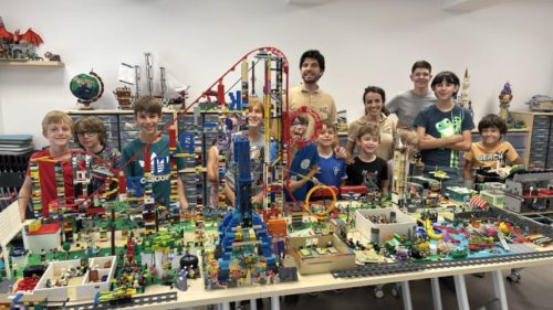 stage vacances lego pédagogie vacances montrant un groupe de participants fiers autour d'un immense parc d'attractions avec montagnes russes.