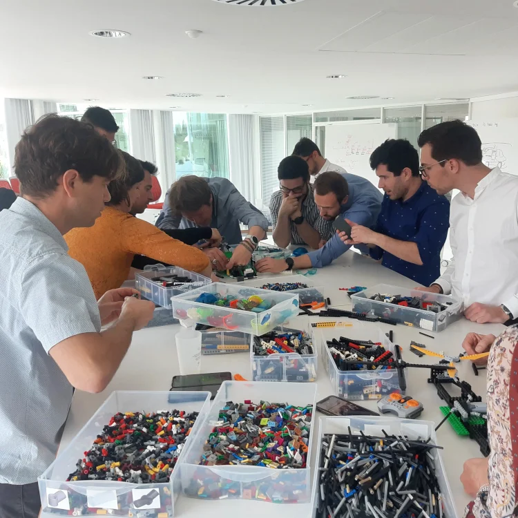 Groupe d'employés très concentrés sur la construction d'un hélicoptère en briques lors d'un atelier collaboratif de séminaire d'entreprise à Toulouse.
